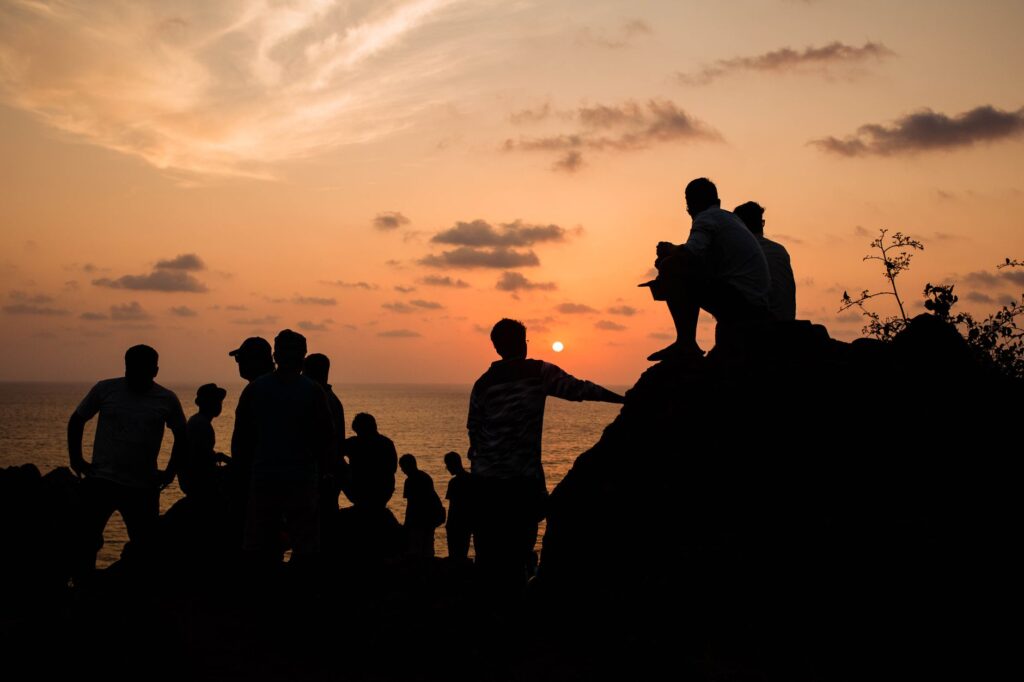 The sunset that money cannot buy: how Energy 52 exposed the hollow luxury of modern Ibiza — crowd watching sunset on rocky beach hands up silhouettes